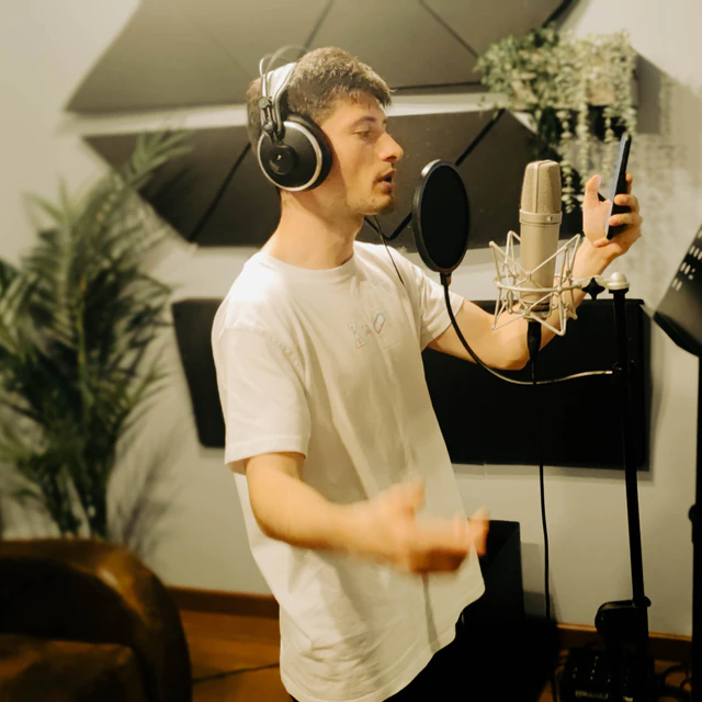 Un cantante interpretando frente al micrófono con auriculares y la letra en el móvil